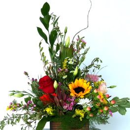 A vibrant and diverse floral arrangement featuring roses, sunflowers, and a selection of other colorful flowers.