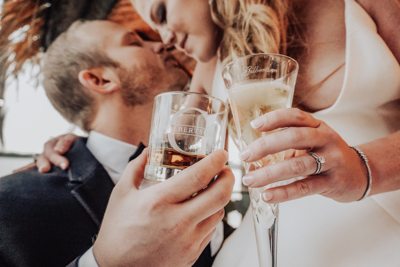 This enchanting photograph by Castaldo Studio features a couple in a heartfelt embrace, sharing a tender kiss while raising their glasses in celebration. Bathed in the perfect lighting, their love shines through as they clink their custom glasses. The attention to detail, from their genuine smiles to the delicate play of light, showcases Castaldo Studio's expertise in capturing intimate moments. The image exudes romance and happiness, a testament to the joyous atmosphere of the occasion. Cheers to love and cherished memories beautifully preserved by Castaldo Studio.