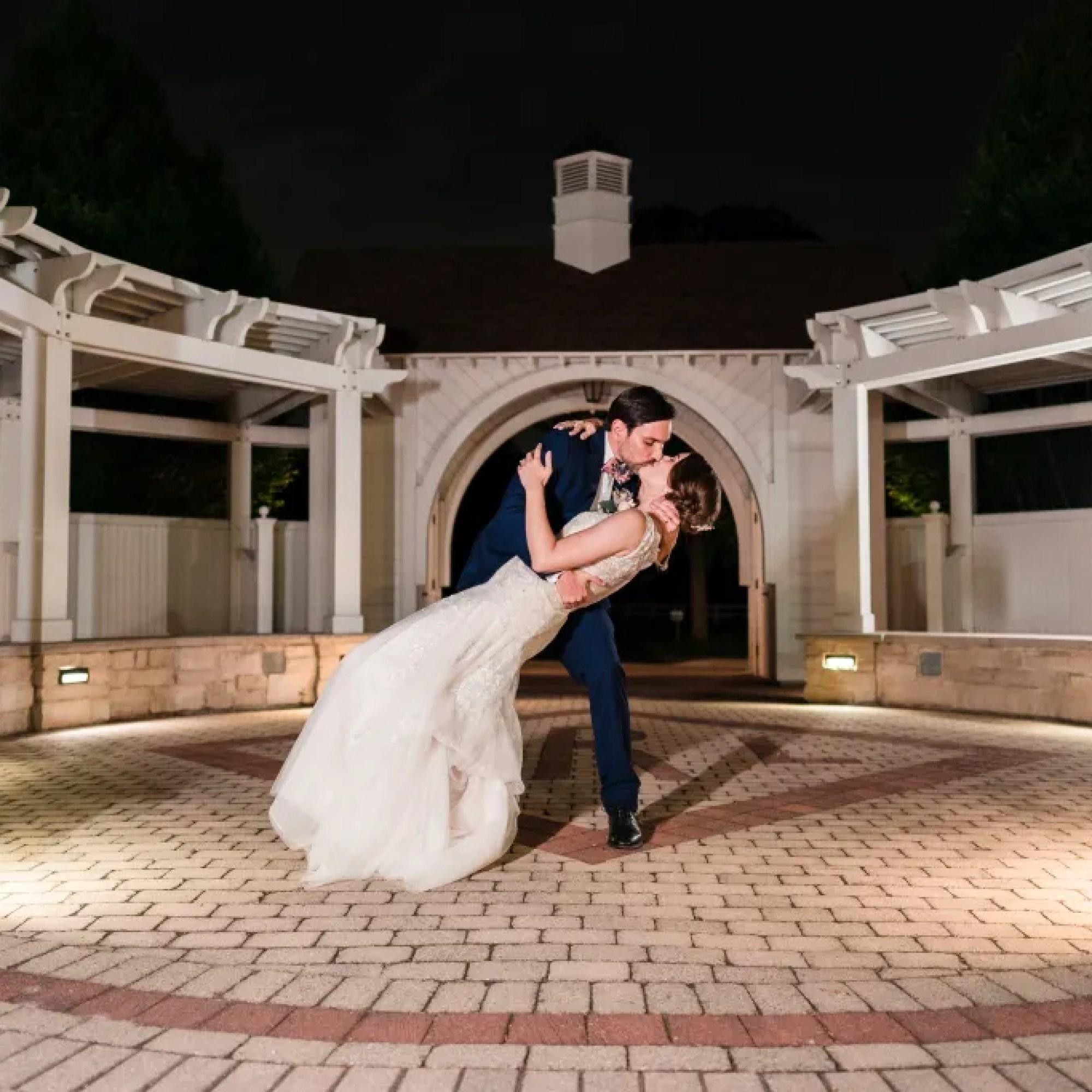 Captivating moment captured by Jerzy Nieves Photography, as the groom dips the bride for a romantic kiss in a picturesque brick courtyard, radiating timeless love and elegance