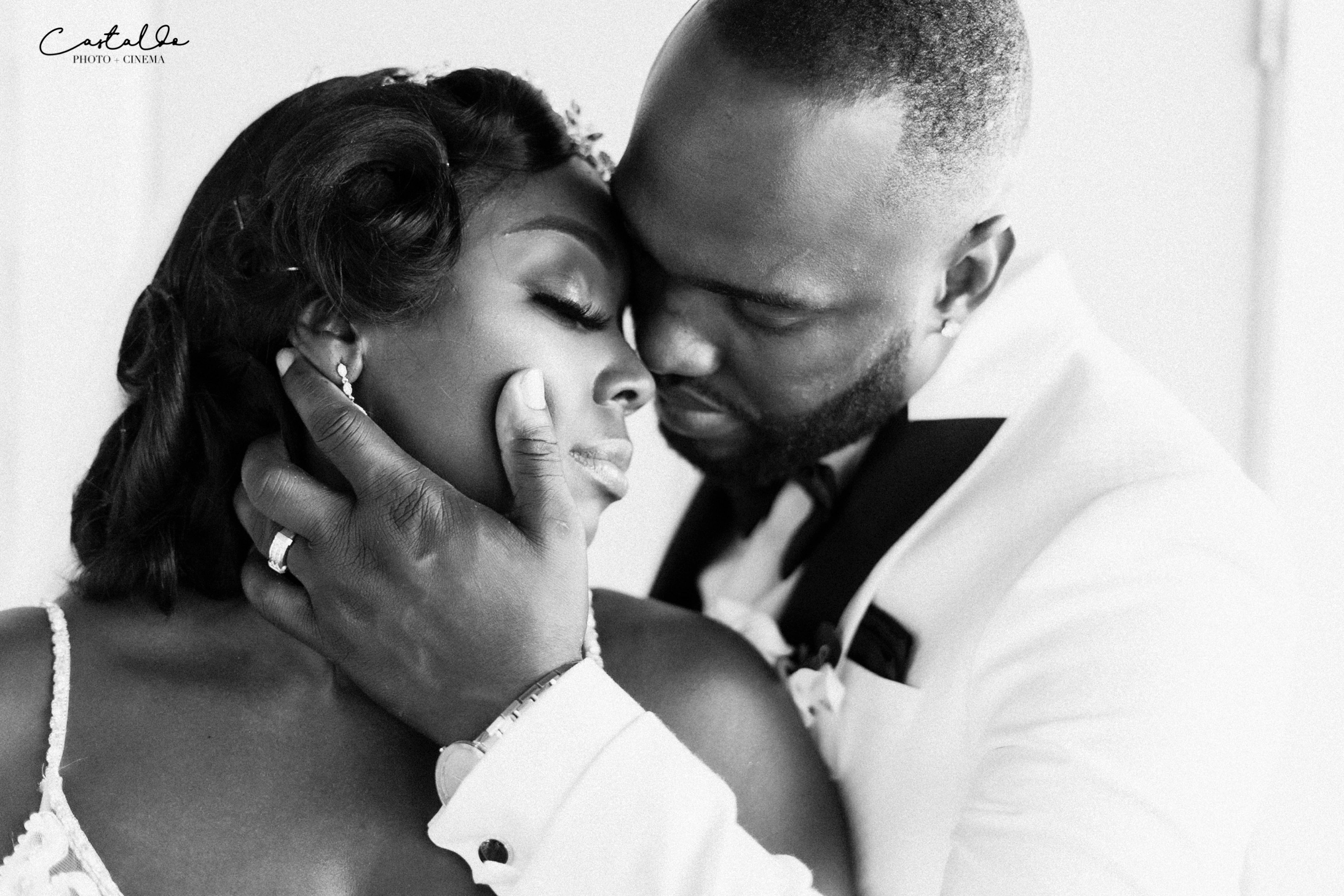 In this stunning black and white photograph captured by Castaldo Studio, a groom passionately holds his bride's face as they lean in for a kiss. The timeless beauty of black and white enhances the intensity of the moment, highlighting their deep connection and overflowing love. The groom's tender grasp and the bride's blissful expression radiate with passion and devotion. This captivating image immortalizes the romantic essence of their special day, capturing the profound bond shared between the couple in a single, unforgettable moment.