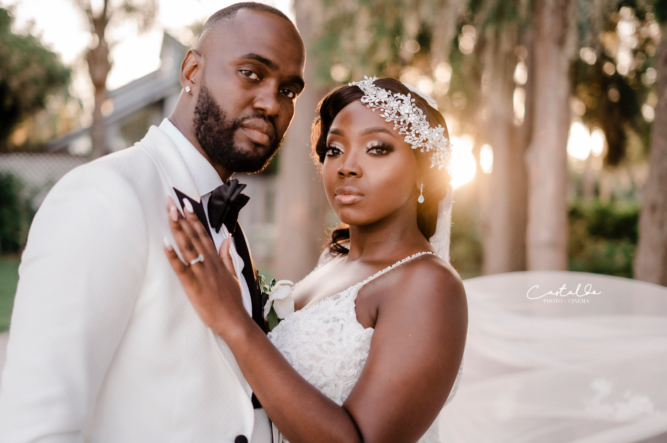 This breathtaking photo by Castaldo Studio features a couple standing together, looking directly at the camera, as the golden rays of the sunset surround them with a warm glow. The perfect lighting accentuates their radiant smiles and showcases the natural beauty of the scene. Against the backdrop of a picturesque sunset, the couple's love shines brightly, symbolizing the beginning of their journey together. This captivating moment captures the essence of their wedding day, filled with joy, romance, and the promise of a lifetime of happiness