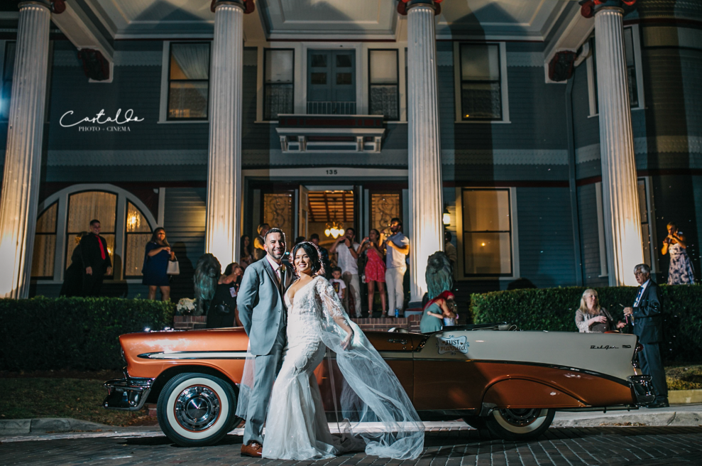 A joyful couple standing in front of a classic car, ready to embark on their journey as husband and wife. This beautiful moment, captured by Castaldo Studio, symbolizes the beginning of their happily ever after. With beaming smiles and excitement in their eyes, they are about to ride off into the sunset, starting a new chapter of their lives together