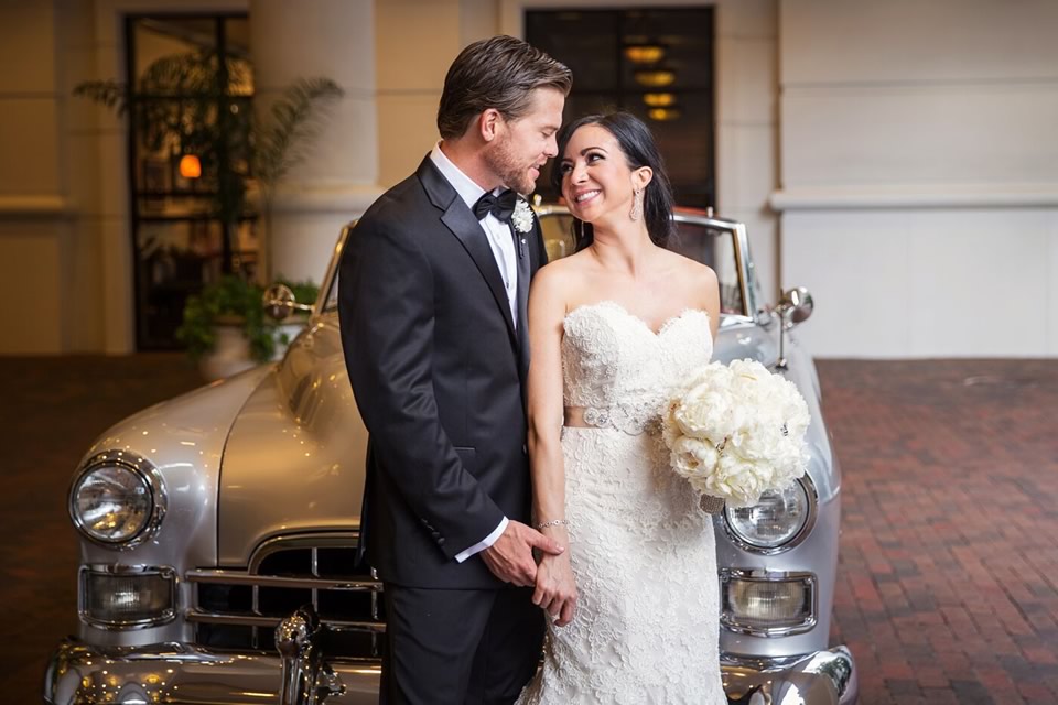 VIP Wedding Transportation: Bride and groom pose in front of a 1948 Cadillac Convertible, looking into each other's eyes