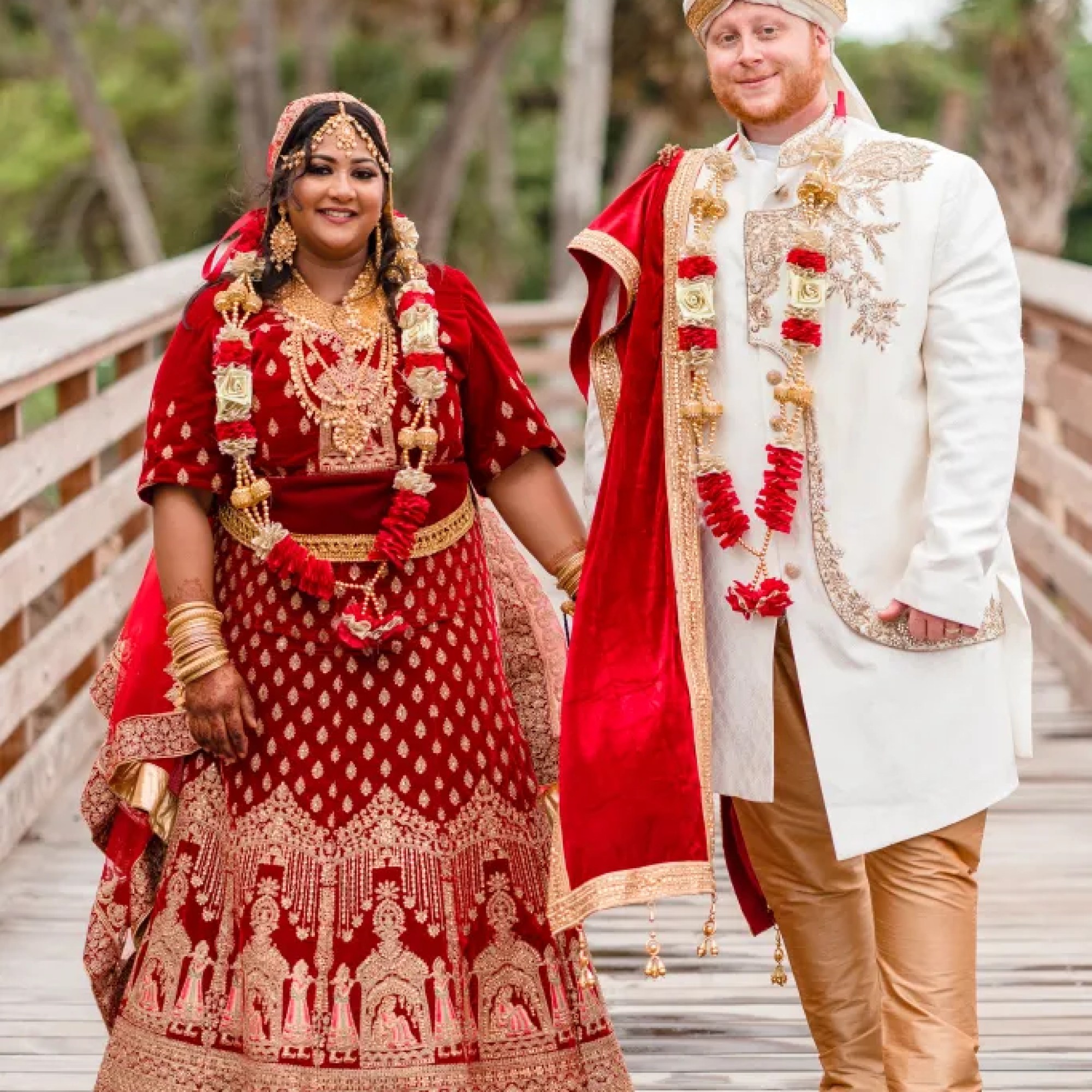 Jerzy Nieves Photography - Happy couple, dressed in traditional Indian wedding attire, holding hands on a beautiful bridge, radiating joy and love at All Inclusive Weddings Orlando