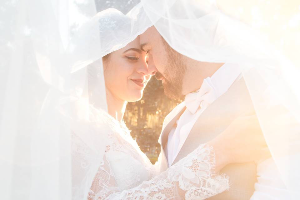 A captivating and intimate photo captured by Castaldo Studio, featuring the bride and groom standing close together under a veil. They share a romantic gaze, their eyes locked with deep affection and love. Embracing each other tenderly, they create a timeless moment filled with romance and connection