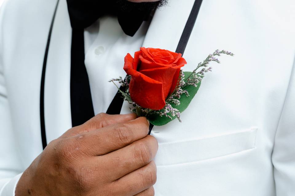 Close-up of a red flower pinned on the white vest of a male, adding a sophisticated and stylish touch to his attire.