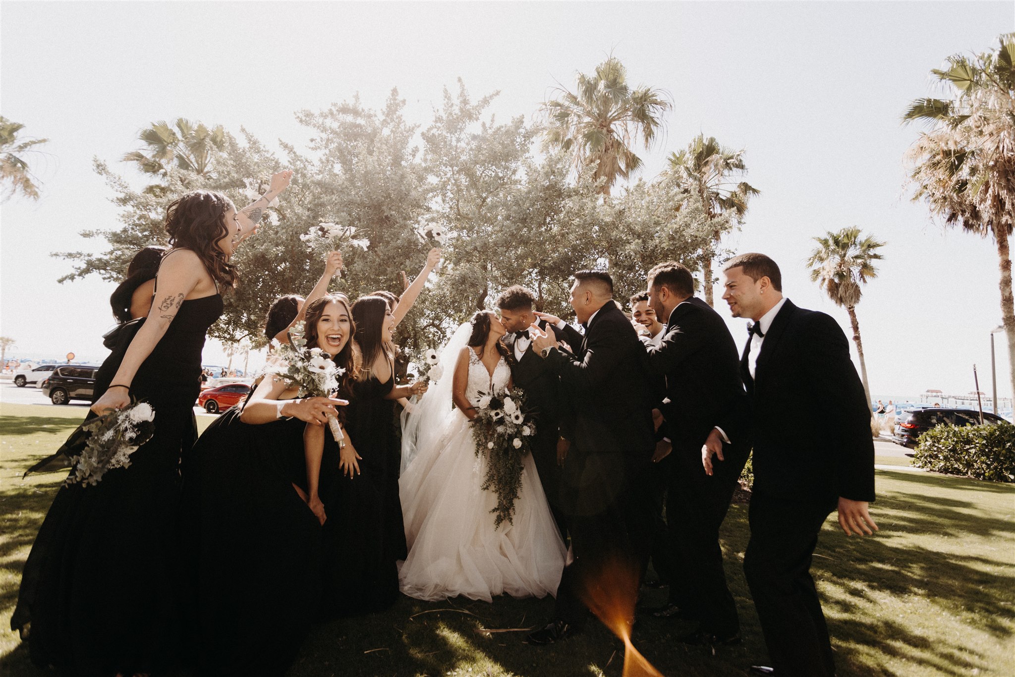 Captured in a tender moment, the bride and groom share a passionate kiss behind a magnificent wooden altar beautifully adorned with bouquets of vibrant flowers. The scene is set against a breathtaking backdrop of a flower-filled oasis, with lush palm trees and glistening water adding to the enchanting ambiance. Created by Simply Enchanted Events, the floral arrangements exude elegance and natural charm, harmonizing perfectly with the surroundings. Love and nature intertwine in this mesmerizing moment at All Inclusive Weddings Orlando.